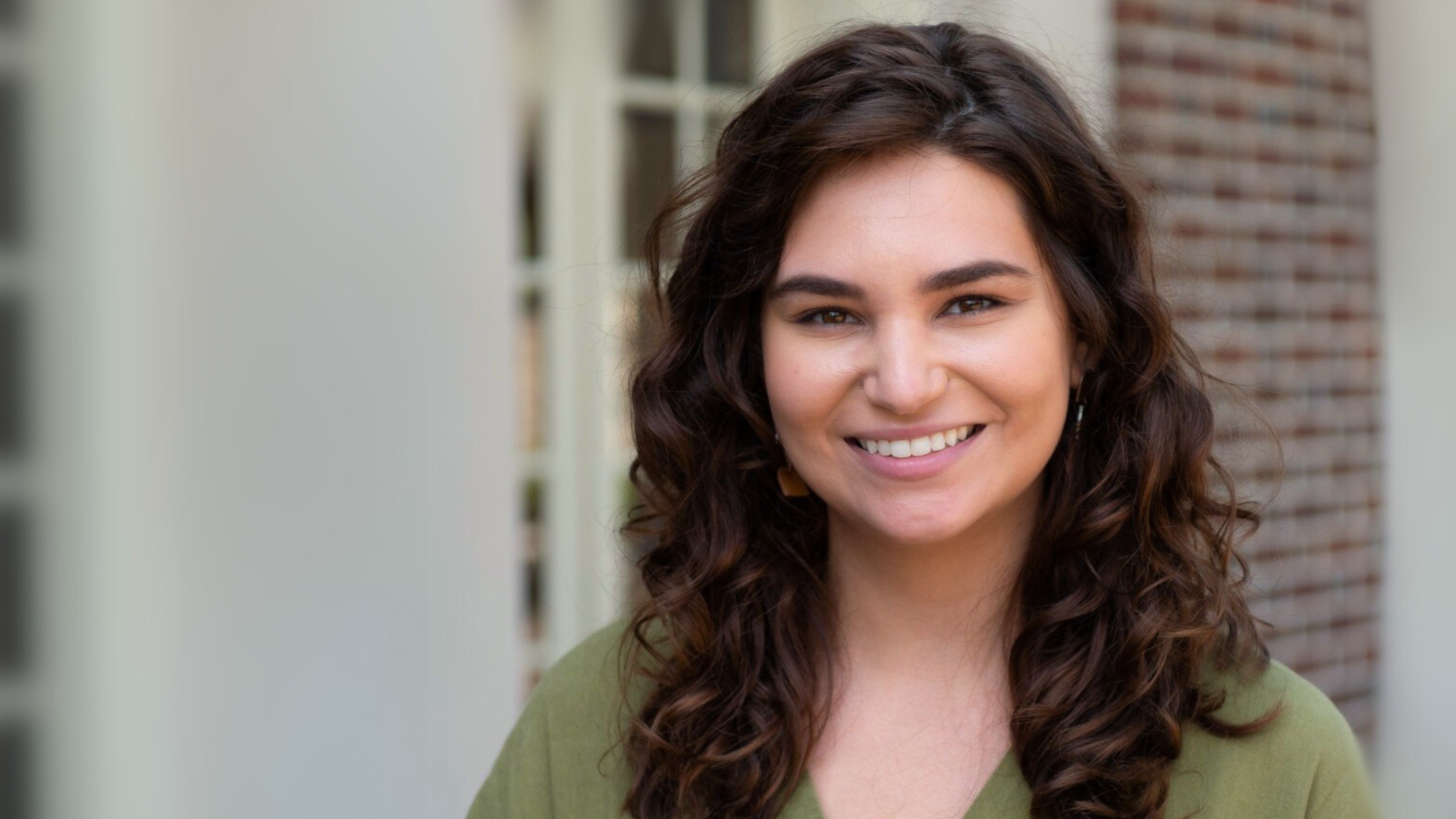 Jessi Wright is wearing green and smiling in front of a brick building.