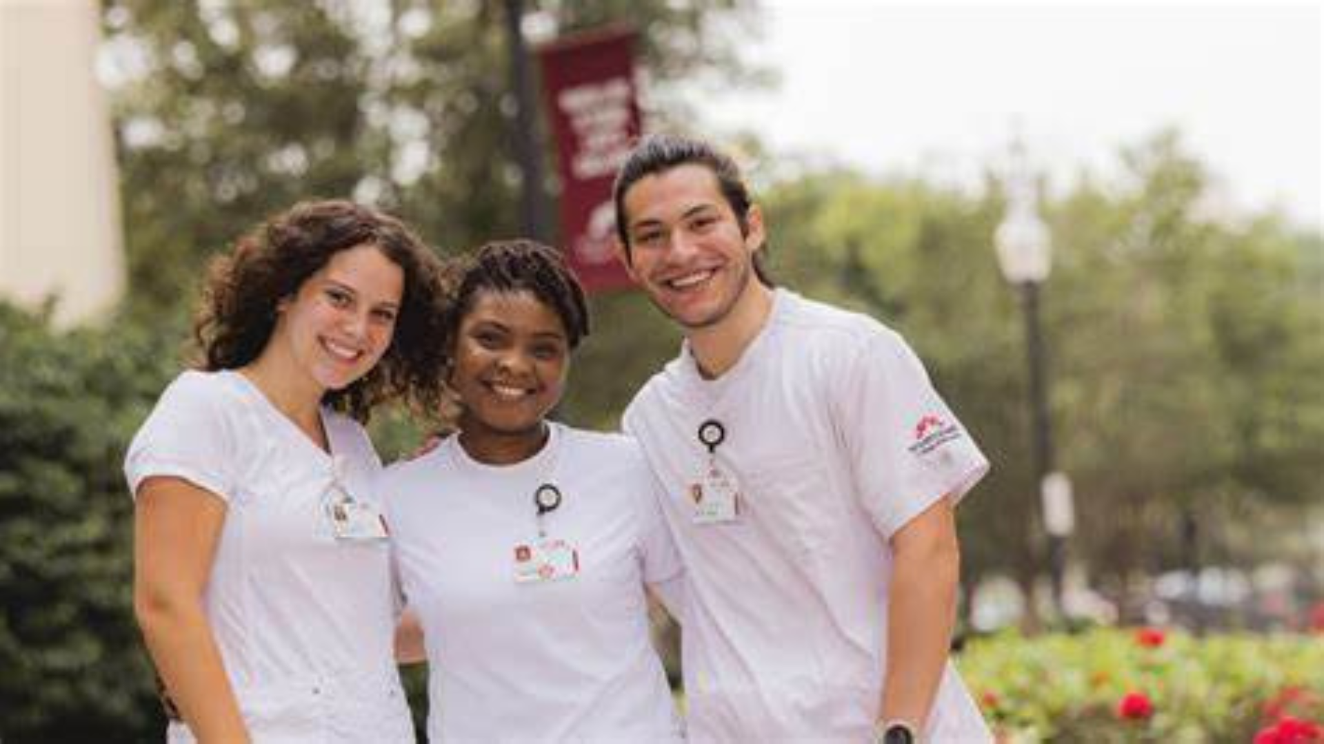 Mount Carmel College of Nursing. Three nurses smile outside of collegiate building.