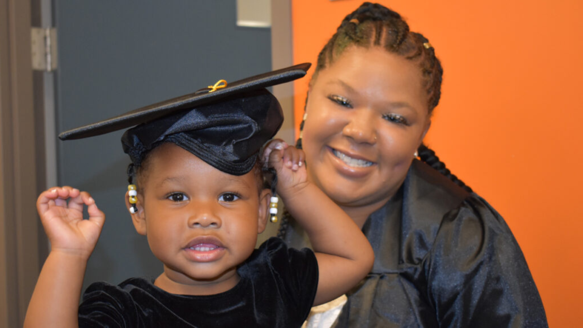 Graduate mother smiles with daughter who wears her graduation cap.
