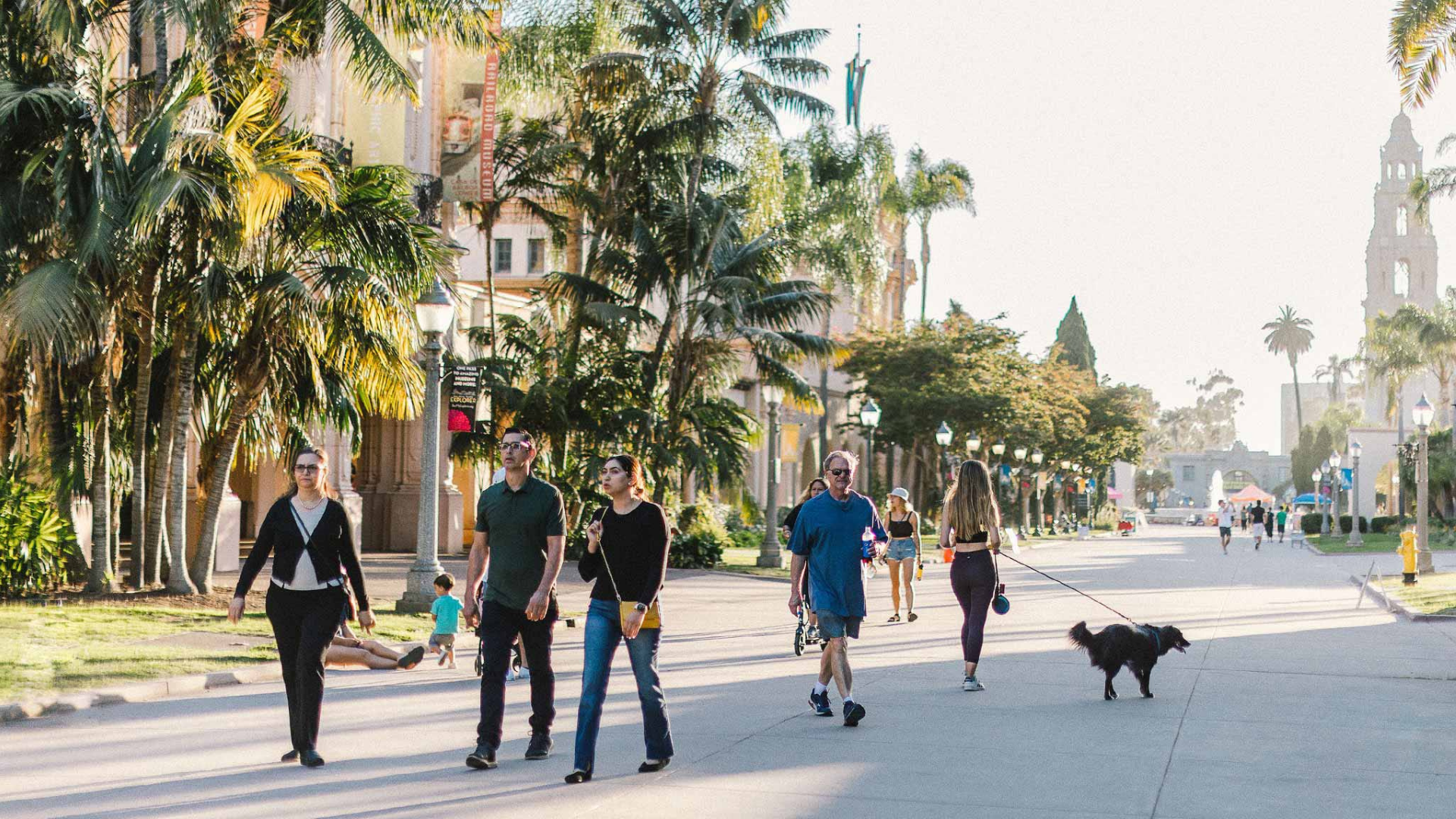 Balboa Park Conservancy. Image shows people walking down a scenic street.