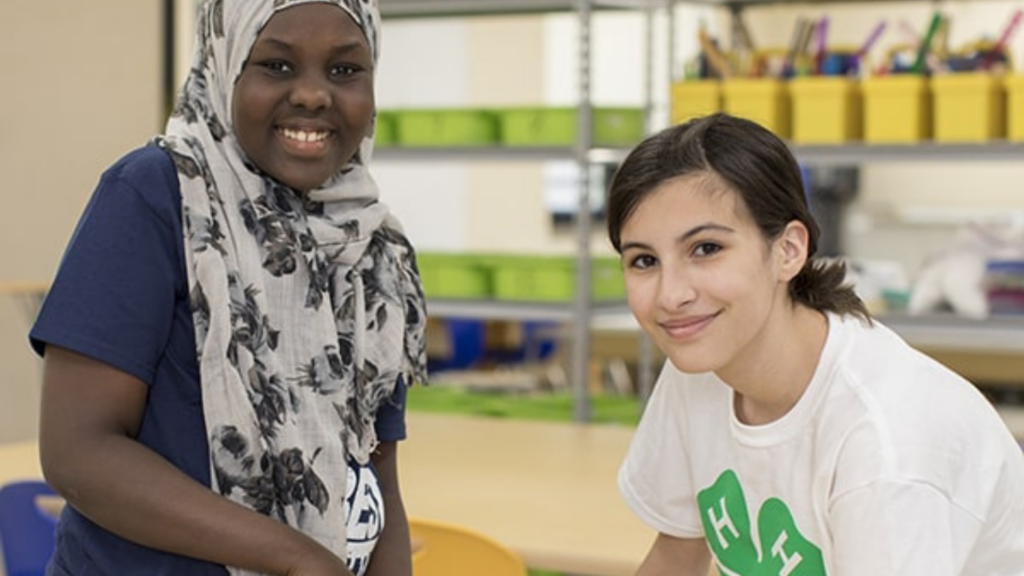 National 4-H Council. Image shows two girls working on a project.