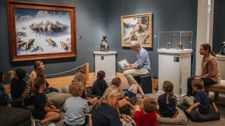 National Museum of Wildlife Art. Image shows a worker reading a book to children in front of an exhibit.