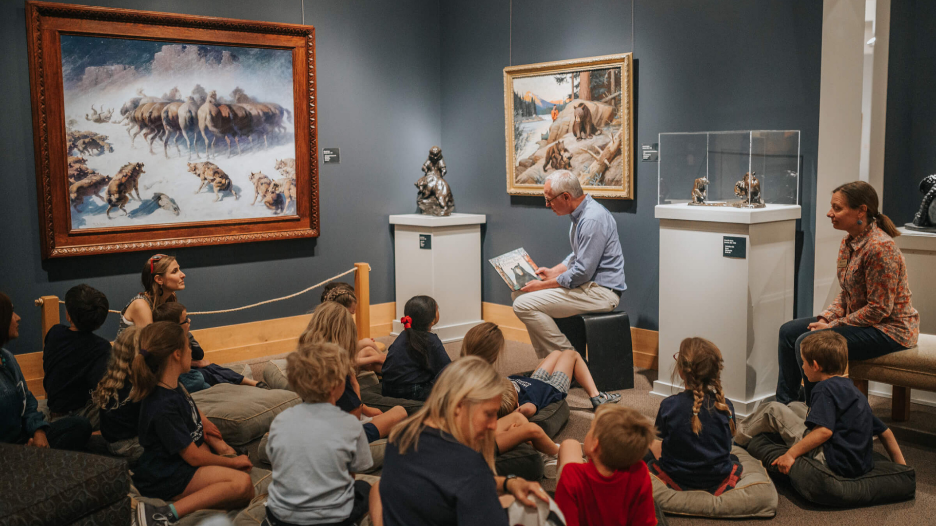 National Museum of Wildlife Art. Image shows a worker reading a book to children in front of an exhibit.