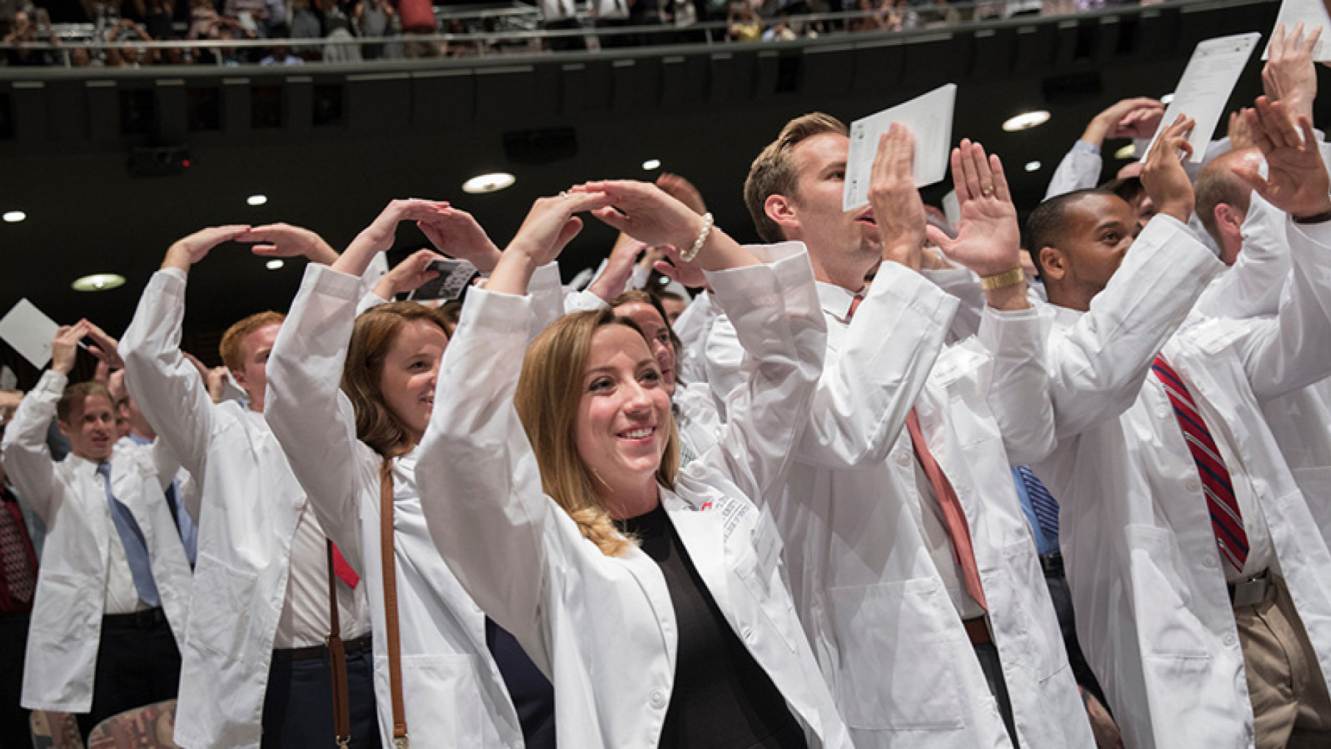 The Ohio State University College of Dentistry. Image shows graduates during a commencement ceremony forming an O shape with their arms.