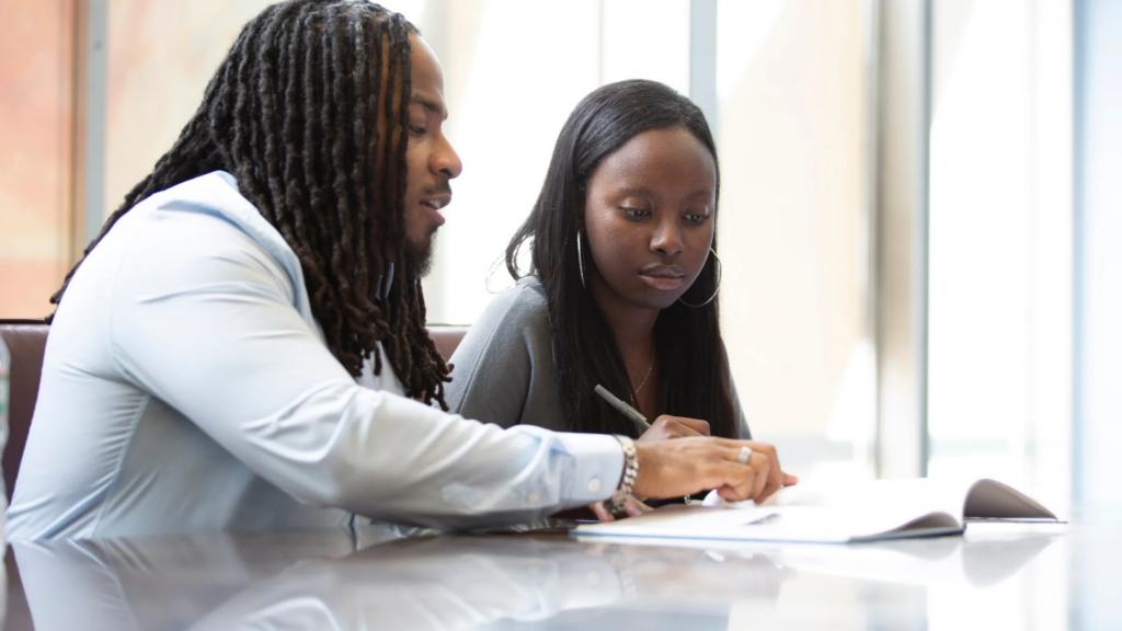 Bottom Line. Image shows an advisor helping a student with a paper.