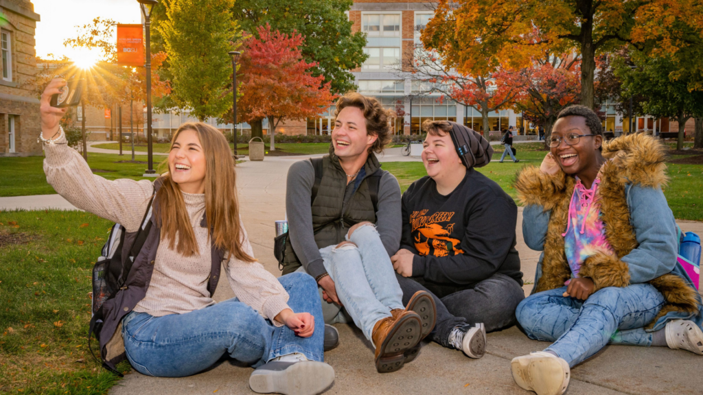 Bowling Green State University. Image shows a group of friends posing for a selfie while sitting on campus grounds.