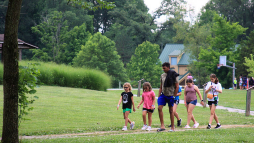 Camp Joy Foundation. Image shows a counselor leading a group of children around camp.