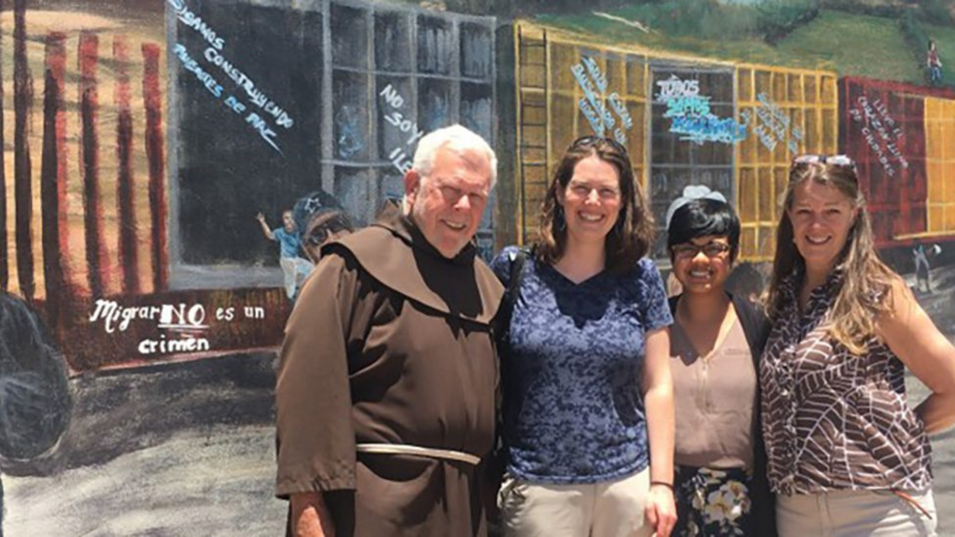 Franciscan Mission Service. Image shows people in front of a mural.