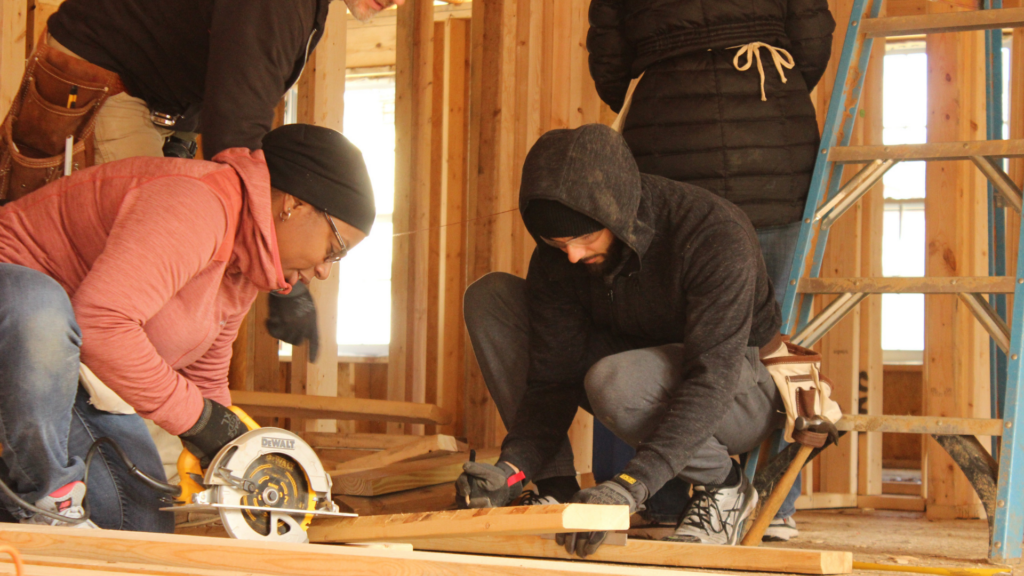 Greater Fredericksburg Habitat for Humanity. Image shows people cutting wood and building a house.