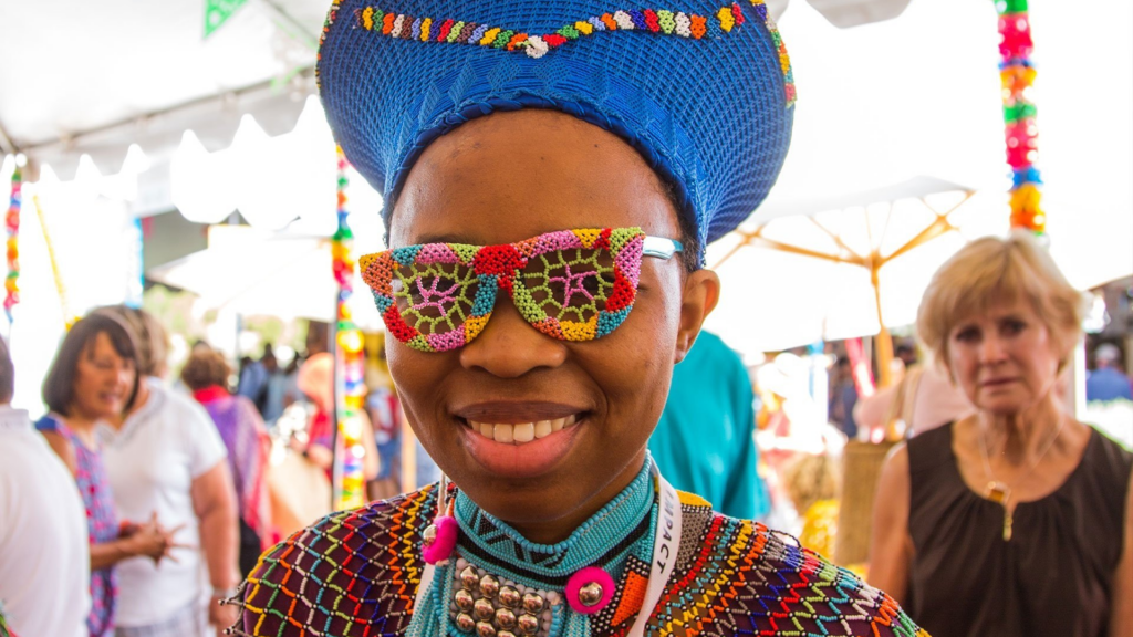 International Folk Art Market. Image shows woman smiling and wearing her colorful woven creations.