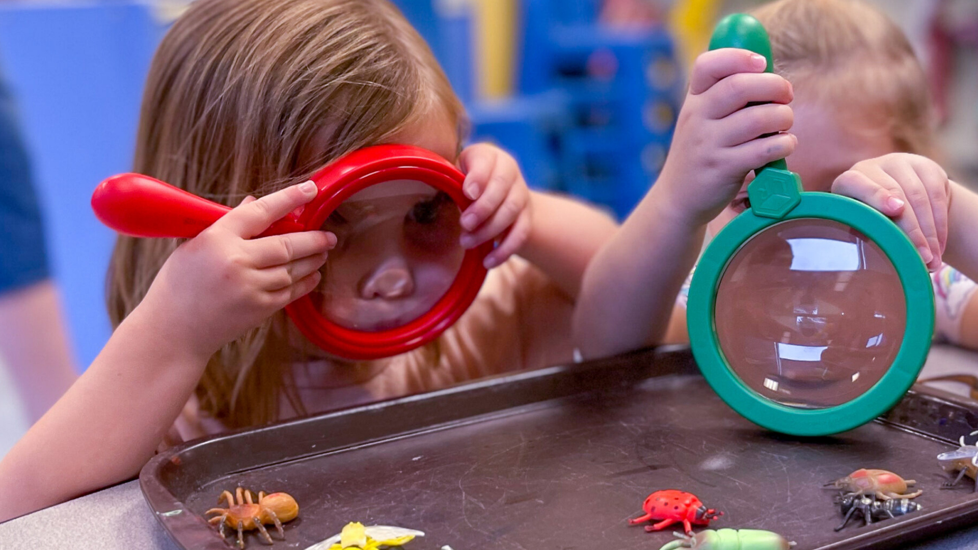 Kids Come First. Image shows children using magnifying glasses to look at toy insects.