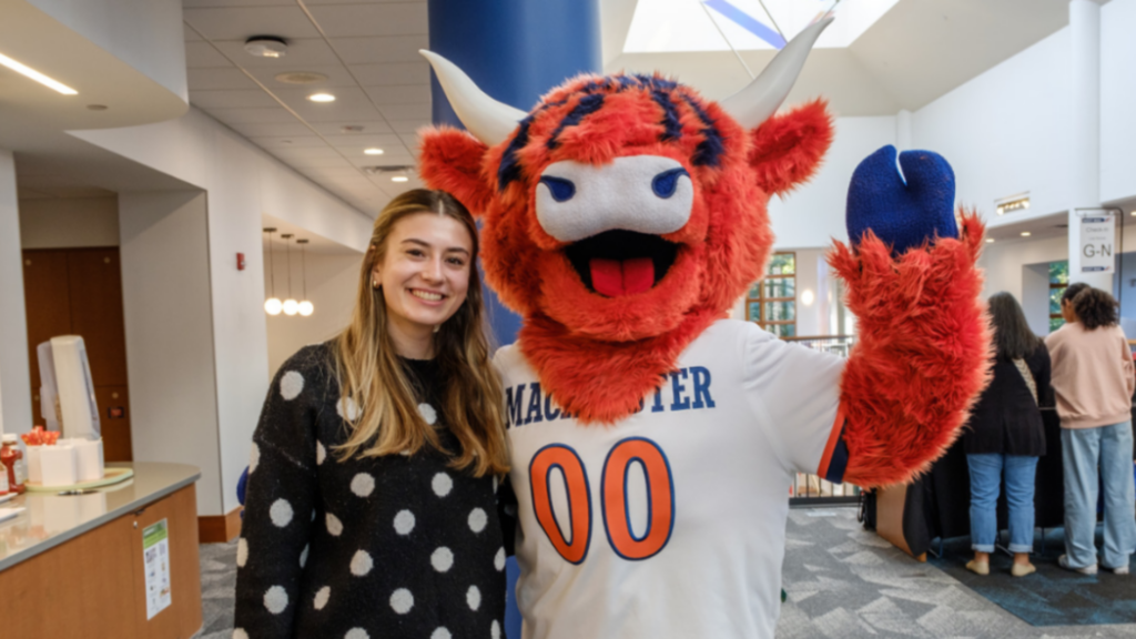Macalester College. Image shows student smiling next to bull mascot.